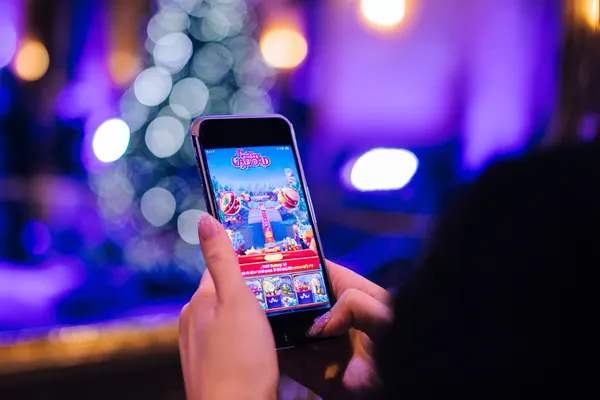 Uma jovem relaxando com o celular enquanto elementos dinâmicos de cassino flutuam ao seu redor, ilustrando a experiência móvel fluida oferecida pelo app FADARICA777.